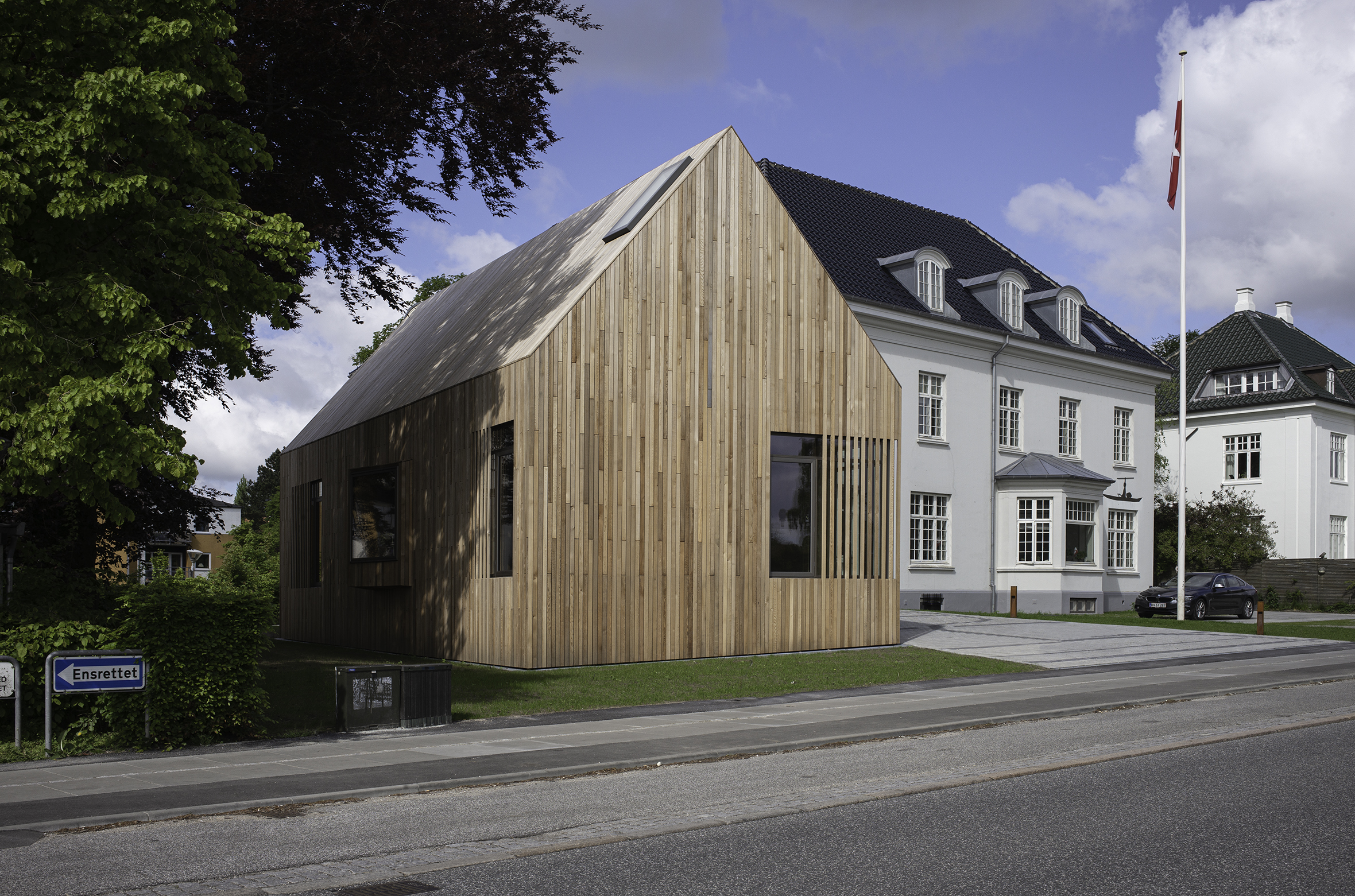 Tilbygningen med træfacade foran smuk hvid villa og flagstang med Grønlands flag