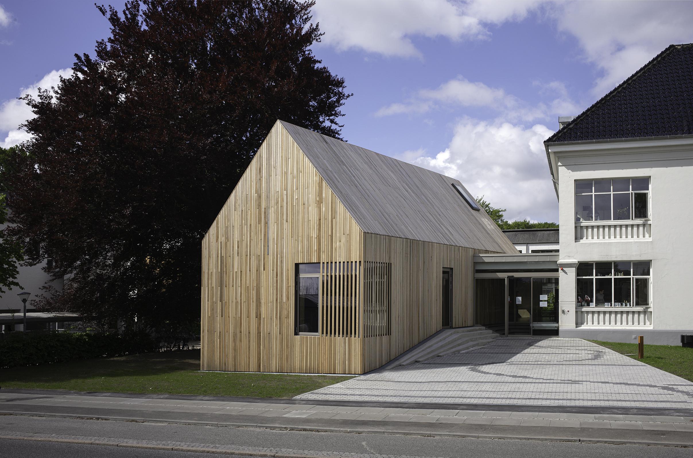Tilbygningen med træfacade foran smuk hvid villa