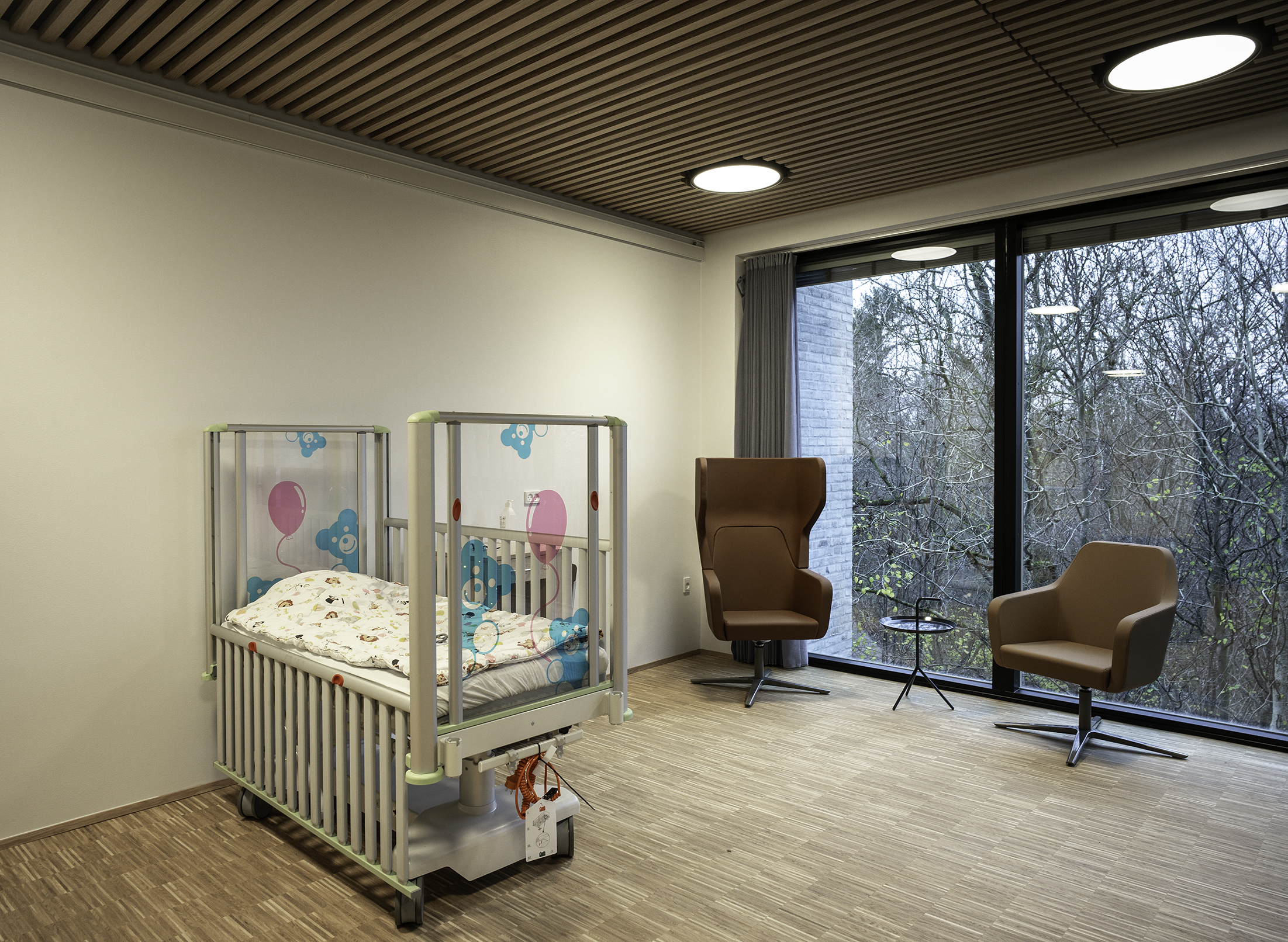 Værelse med sygehusseng til spædbarn og trælameller i loft