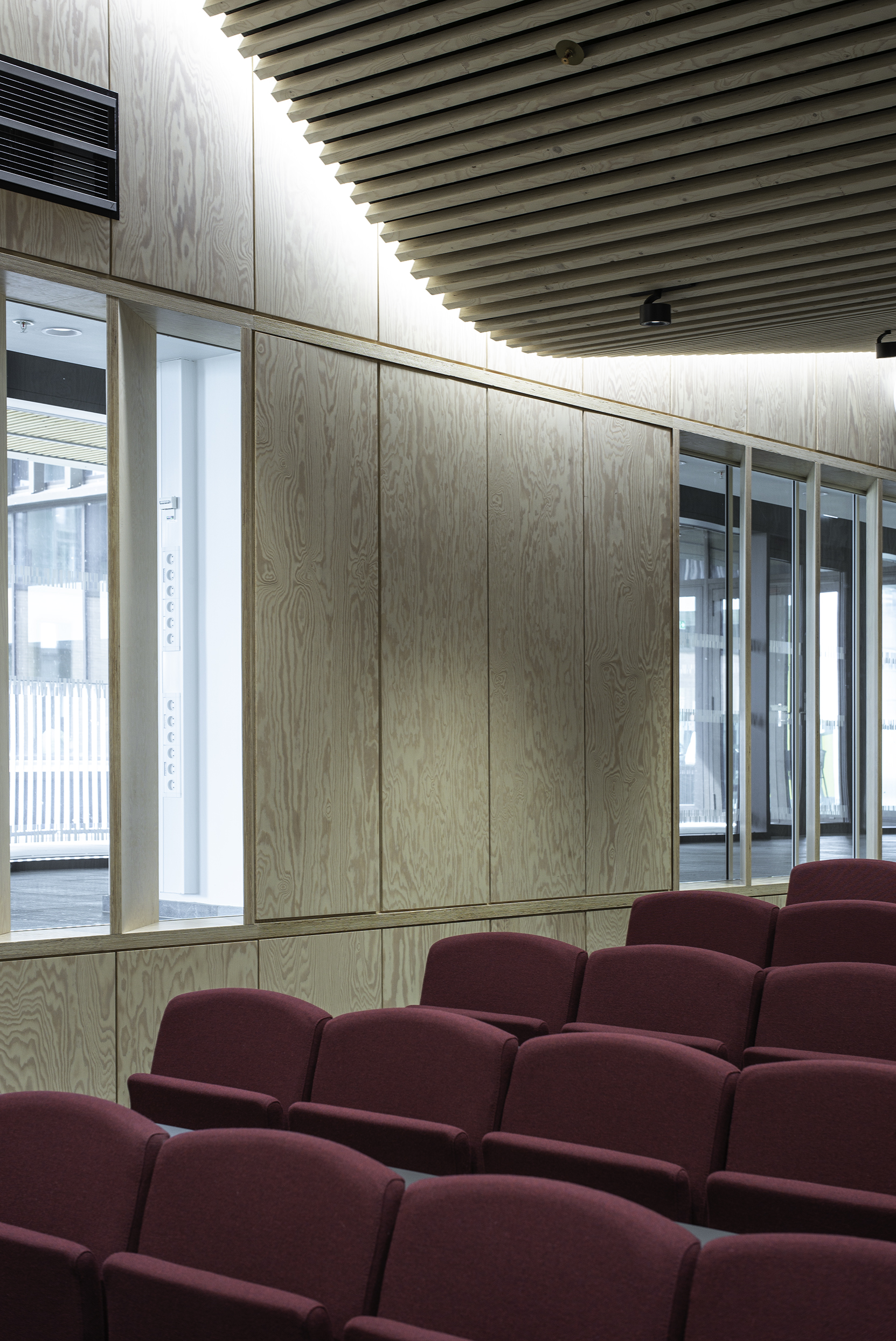 Foredragssal med glatte træpaneler på vægge med flere vinduer og vinrøde stole