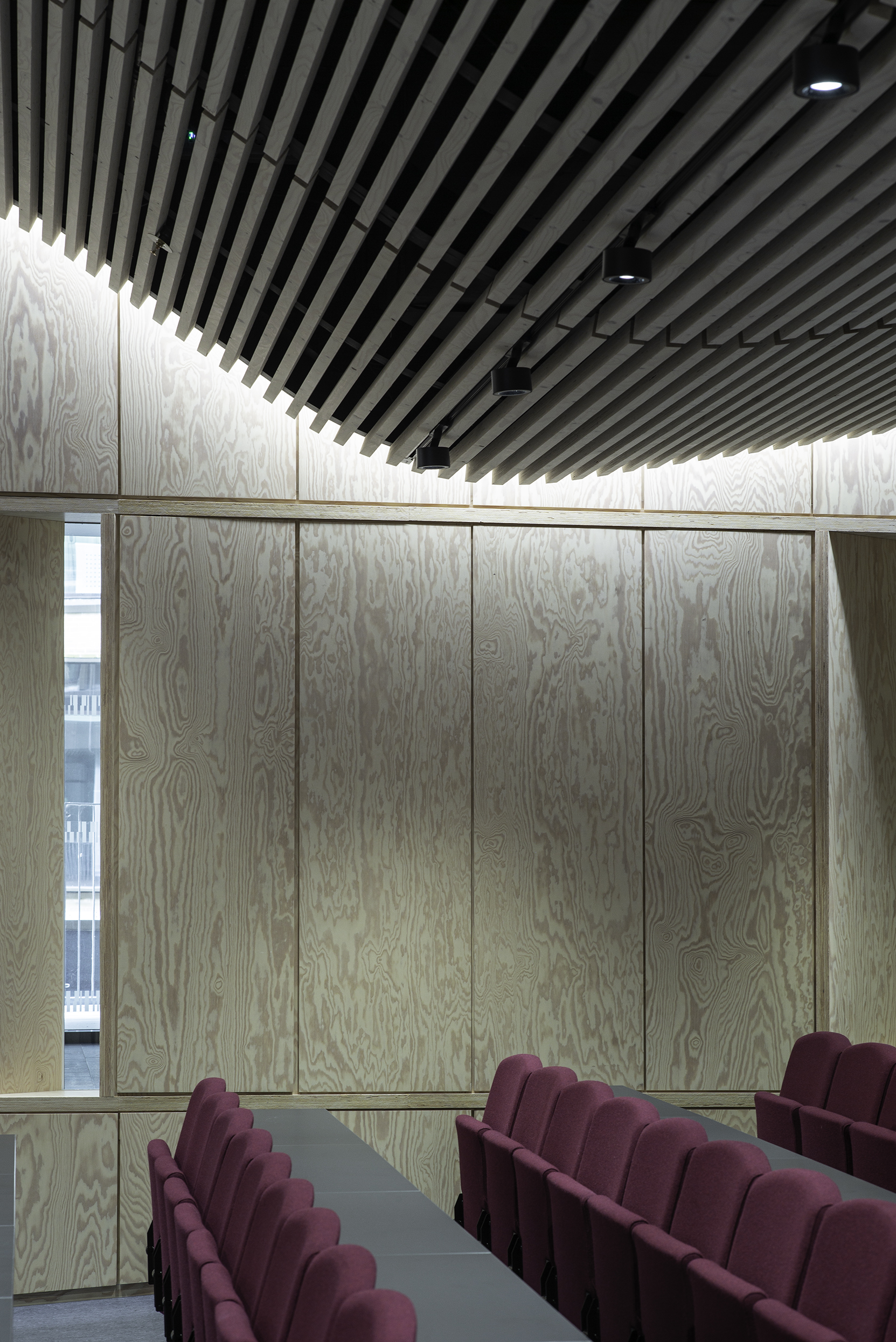 Foredragssal med glatte træpaneler på vægge og vinrøde stole